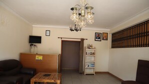 Un hall d’hôtel avec un comptoir d’accueil en bois, des canapés en cuir, une table basse, un lustre, un téléviseur, une bibliothèque et une porte avec un rideau.