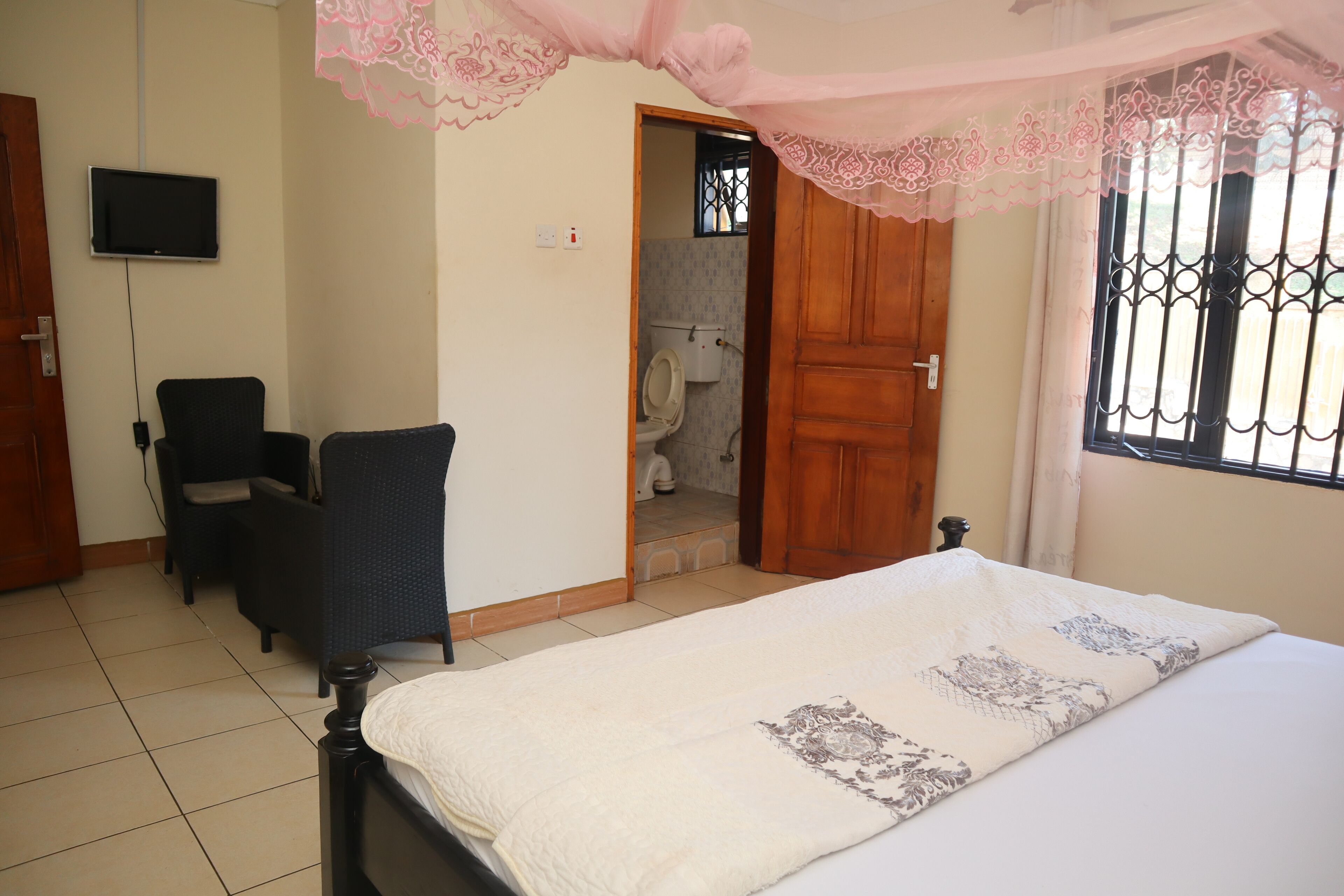 A bedroom with a bed, a chair, a television, and a bathroom visible through an open door.