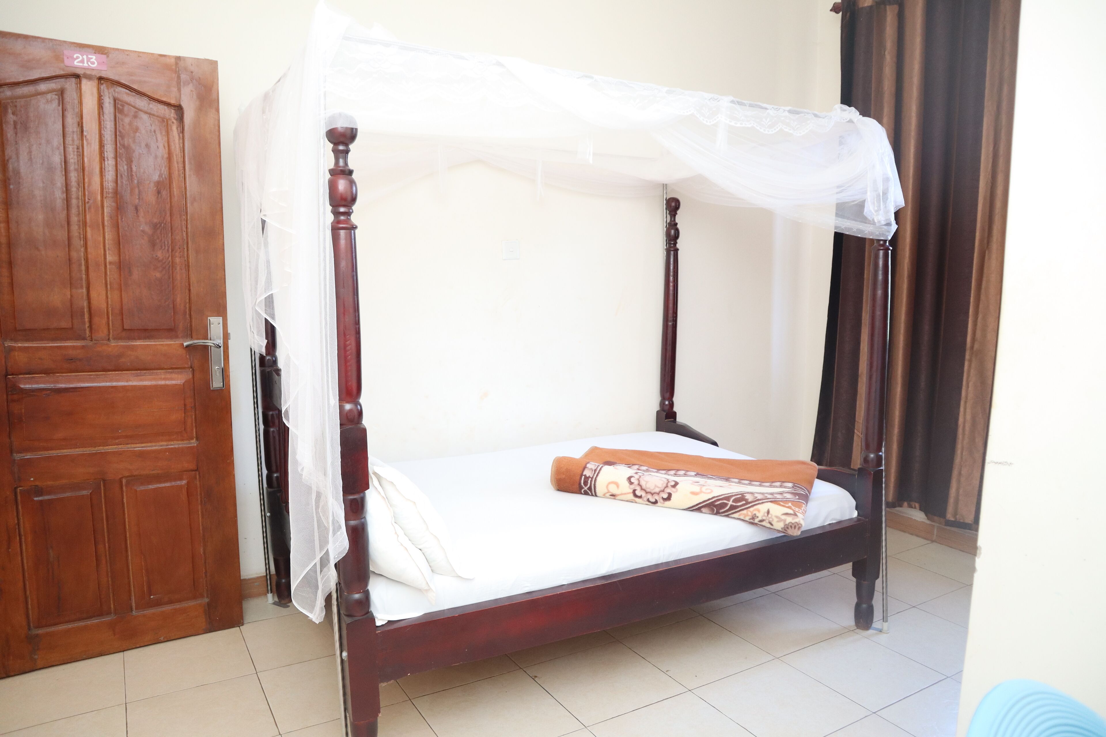 A wooden bed with a canopy, a closed wooden door, and a tiled floor.