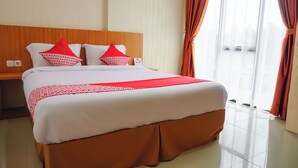A hotel room with a large bed, red and white pillows, a wooden headboard, and a view through a large window. - Hotel O Bukittinggi near Jam Gadang formerly Hotel Aedo (Bukittinggi)