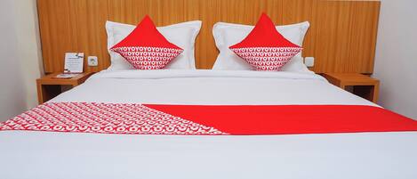 A neatly made bed with a white and red bedspread, two pillows with red and white patterns, and a wooden headboard.