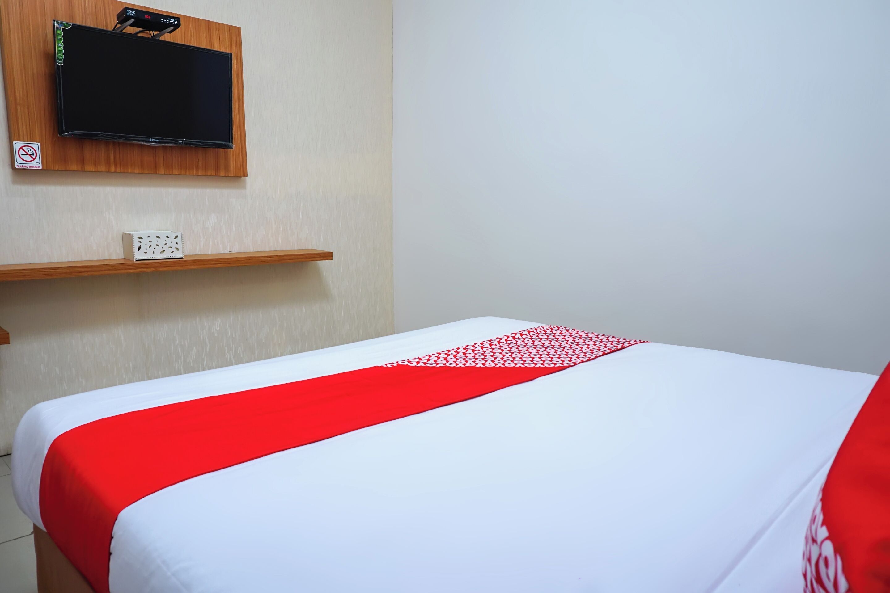 Ein Hotelzimmer mit einem Bett, einem Wandfernseher und einem Regal mit einem kleinen Gegenstand.