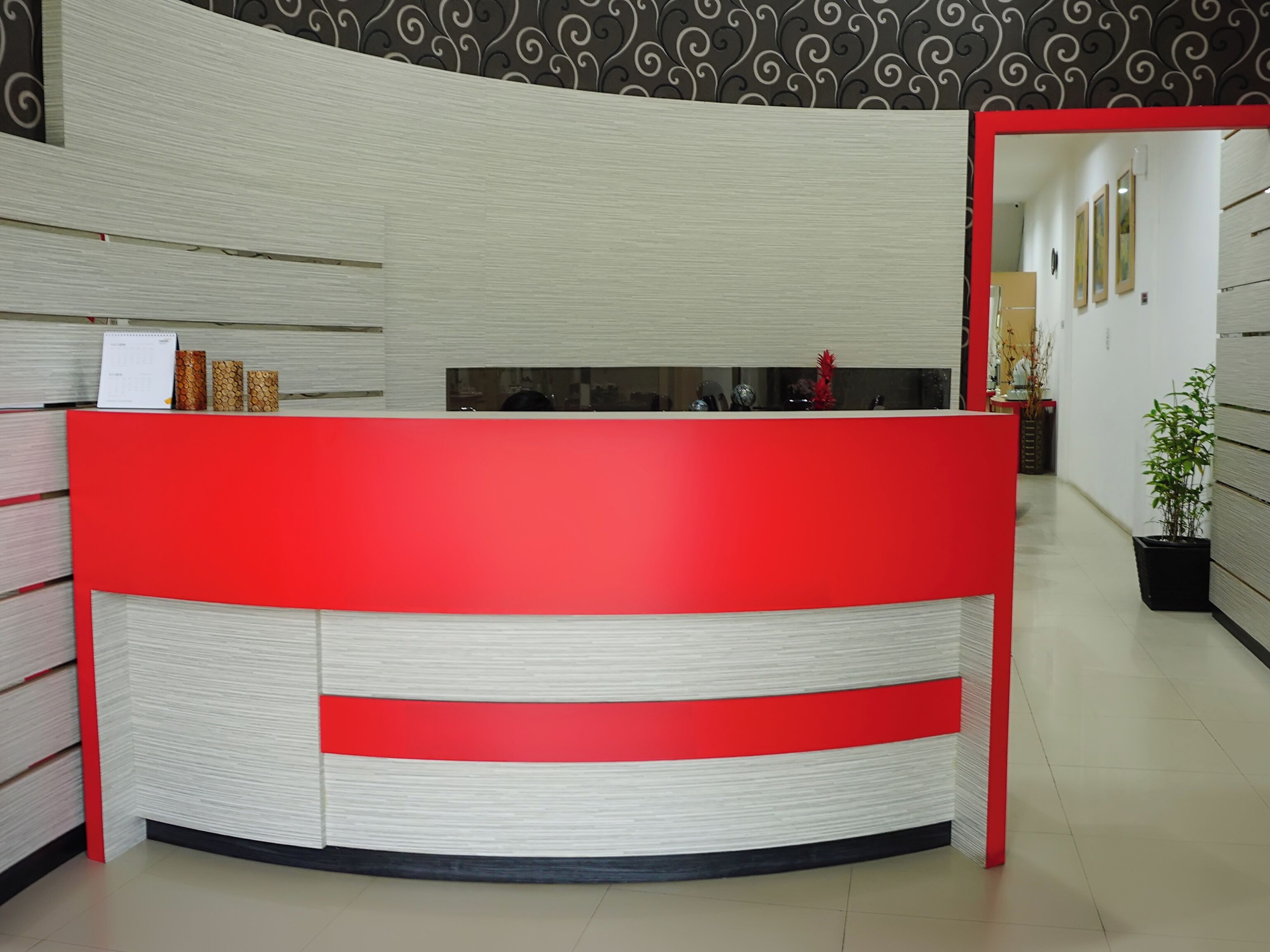 A reception desk with a red and white design, a patterned wall in the background, and a potted plant to the right.