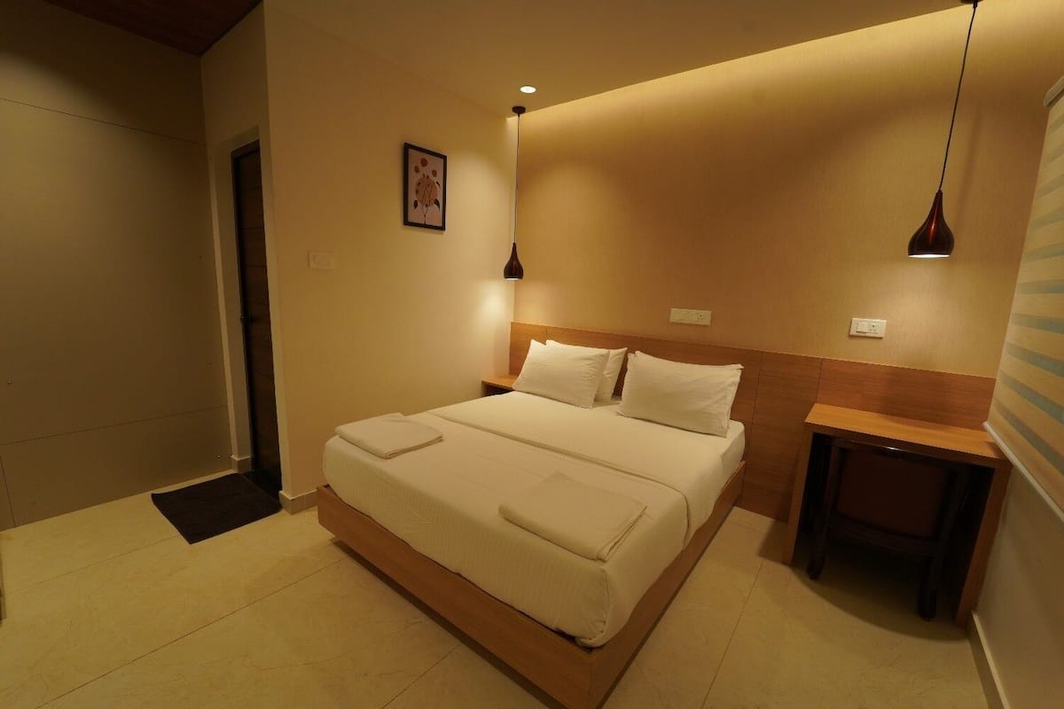 A neatly arranged bedroom with a bed, bedside tables, a nightstand, a framed picture on the wall, and a hanging light fixture.