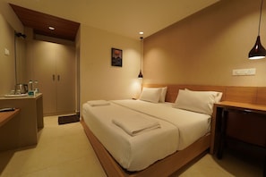 A hotel room with a double bed, bedside tables, a desk with a chair, a wardrobe, and a painting on the wall.