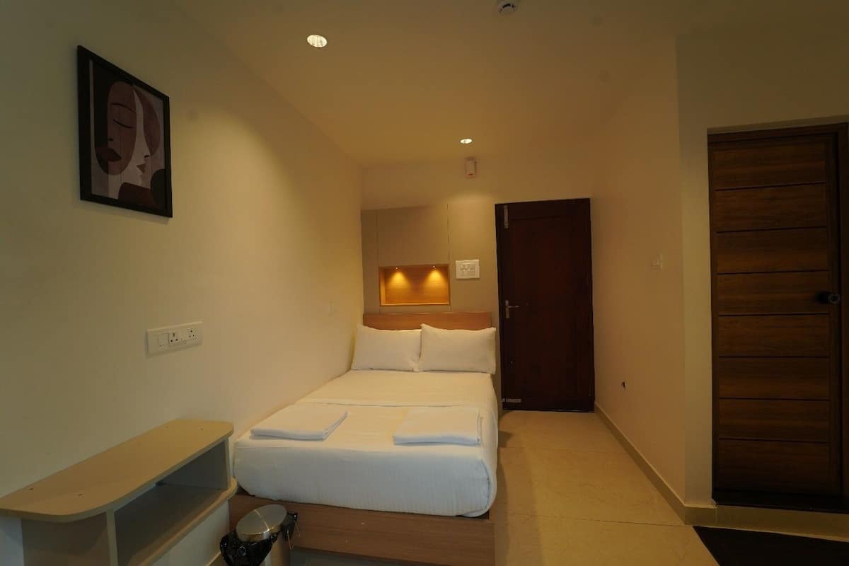 A hotel room with a bed, bedside table, wall-mounted light, and a door.