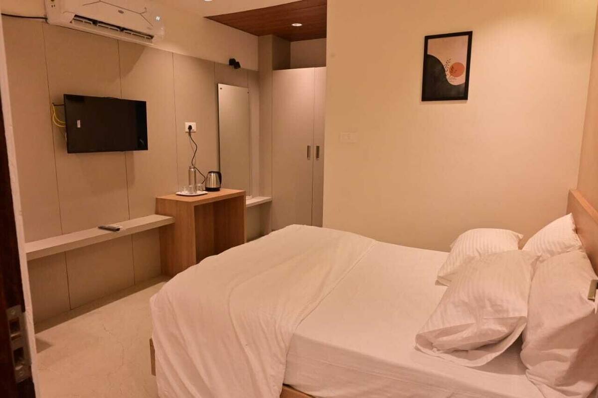 A bedroom with a bed, a TV, a mirror, a wardrobe, and a small table with a kettle.