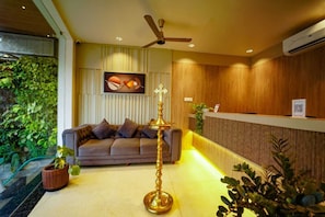 A reception area with a sofa, a decorative lamp, and a wall-mounted air conditioning unit. - Saba's Courtyard (Colachel)