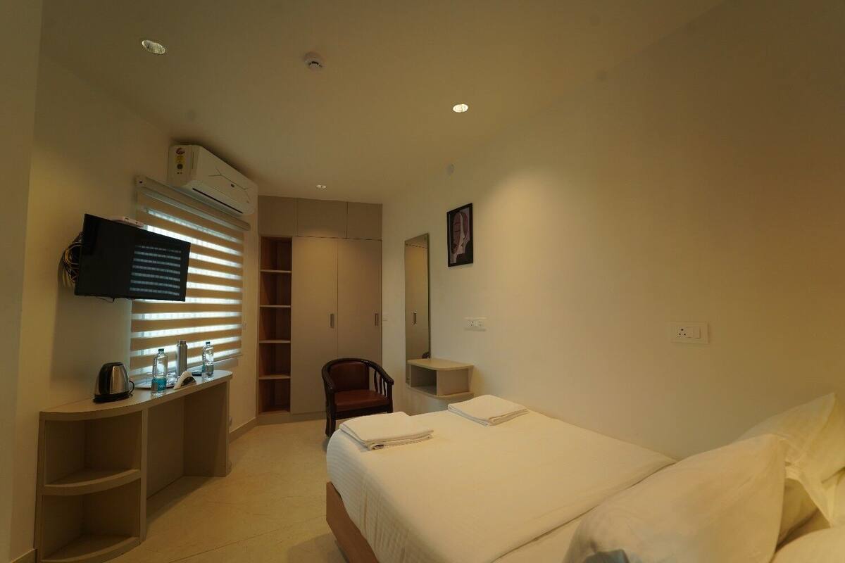 A hotel room with a bed, a desk with a flat-screen TV, a chair, a wardrobe, and a mirror.