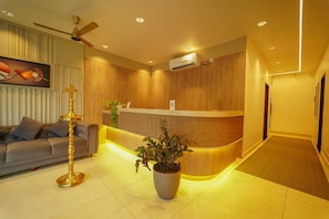 A reception area with a wooden reception desk, a sofa, a floor lamp, and a potted plant.