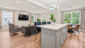 Una cocina moderna con una isla central, un comedor con sillas y un televisor montado en la pared.