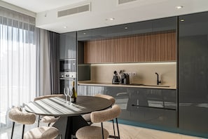 A modern kitchen with a round dining table, cushioned chairs, and built-in appliances. - Mercury Suite Designer Apartment with Pool Access (San Ġiljan)