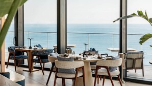 A modern dining area with large windows overlooking the sea, featuring contemporary furniture and a view of the ocean. - Mercury Suite Designer Apartment with Pool Access (San Ġiljan)