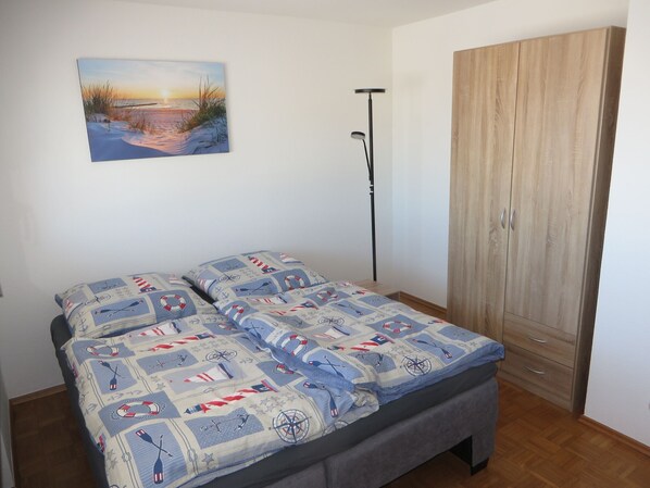 A bedroom with a bed, a wardrobe, a floor lamp, and a painting on the wall.