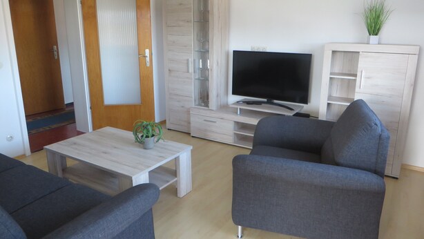A modern living room with a flat-screen TV, grey sofas, a wooden coffee table, and a cabinet with glassware. - Apartment 'City View' with Private Terrace and Wi-Fi (Bräunlingen)
