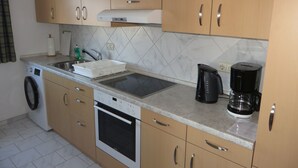 A kitchen with wooden cabinets, a built-in oven, a washing machine, a sink, and a coffee maker. - Apartment 'City View' with Private Terrace and Wi-Fi (Bräunlingen)