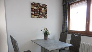 A dining area with a table and chairs, a potted plant, a window with curtains, and a wall-mounted artwork. - Apartment 'City View' with Private Terrace and Wi-Fi (Bräunlingen)