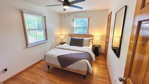 Quarto com cama, duas mesas de cabeceira, um ventilador de teto e duas janelas com persianas.