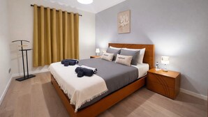 Una camera da letto moderna con un letto di legno, due comodini con lampade, un lampadario e un'ampia finestra con tende.