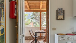 An open doorway leading to a balcony with a table and chairs, a washing machine, and a fire extinguisher. - Casa Bouganvillea con Terrazza by Wonderful Italy (Isola delle Femmine)