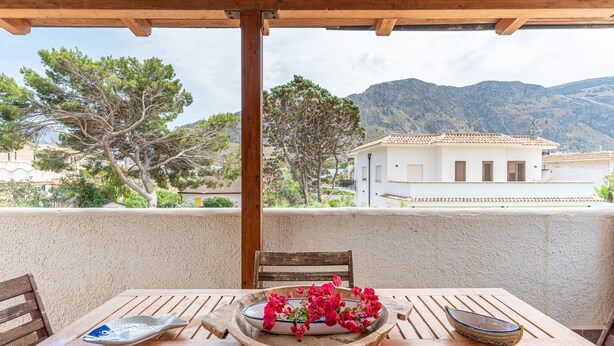 A wooden table with a bowl of flowers, a fish-shaped plate, and a bowl on a balcony overlooking a mountainous landscape. - Casa Bouganvillea con Terrazza by Wonderful Italy (Isola delle Femmine)