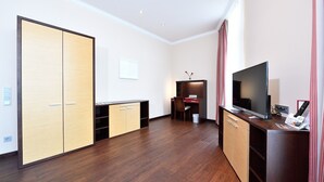 A hotel room with a wooden floor, a TV, a desk with a chair, and a wardrobe. - Spacious 2-person suite with lake view (Heimbach)