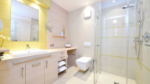 A modern bathroom with a glass-enclosed shower, a large mirror, and a vanity with a sink and storage. - Spacious 2-person suite with lake view (Heimbach)