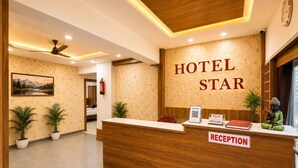 A hotel reception desk with a 'Hotel Star' sign, a reception area, a ceiling fan, and a framed picture on the wall. - STAR HOTEL (Ahmedabad)