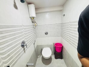 A small bathroom with a toilet, a shower, and a pink bucket.