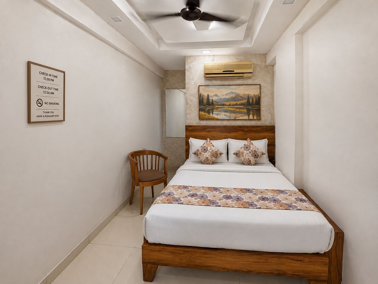 A hotel room with a bed, a chair, a ceiling fan, a painting, and a sign with check-in and check-out times.