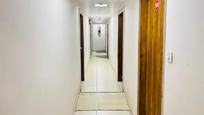 A long, narrow hallway with white walls and a tiled floor. There are wooden doors on both sides, one of which has a red sign with the number 101. - STAR HOTEL (Ahmedabad)