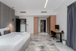 A modern hotel room with a large bed, a desk, and a computer. There is a bathroom visible in the background. - Elegant 2BR w Balcony Walk to JBR Beach (Dubai)