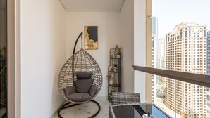 Un balcon agrémenté d’un fauteuil suspendu, d’une petite table, d’une étagère décorative avec des plantes et offrant une vue sur de hauts immeubles.