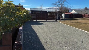 A gravel driveway leading to a fenced area with a building and a mountain in the background. - Omarama Crib – Spotless Scenic Base for Families (Omarama)