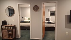 A hotel room with a bed, a bedside table with a lamp, a clock, and a small window. - Omarama Crib – Spotless Scenic Base for Families (Omarama)