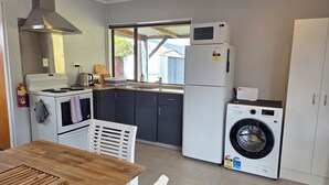 A compact kitchen with a stove, microwave, refrigerator, and washing machine. - Omarama Crib – Spotless Scenic Base for Families (Omarama)