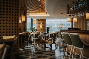Un restaurante con suelo a cuadros, mesas redondas y sillas de respaldo trenzado.