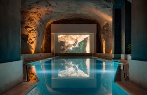 An indoor swimming pool with a rocky cave-like wall and a large projection screen. - Mercury Suite Apartment with Pool Access in St. Julians (San Ġiljan)