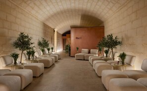 Une pièce spacieuse avec un haut plafond en arc, plusieurs coins salon et des plantes en pot.