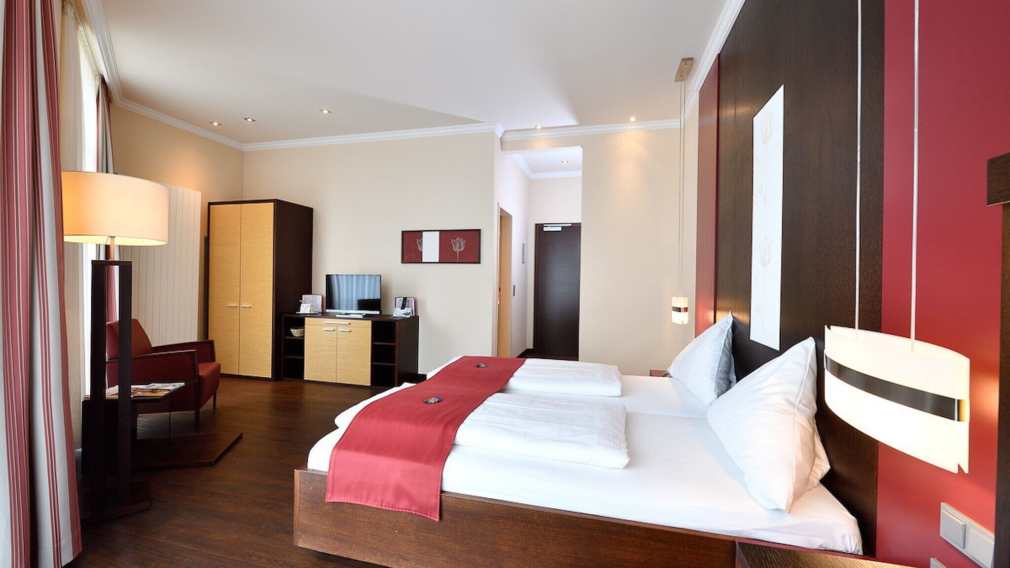 Een hotelkamer met een groot bed, een bureau met een computer, een kledingkast en een televisie.
