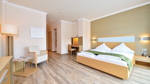 A hotel room with a large bed, a desk, a chair, and a lamp.