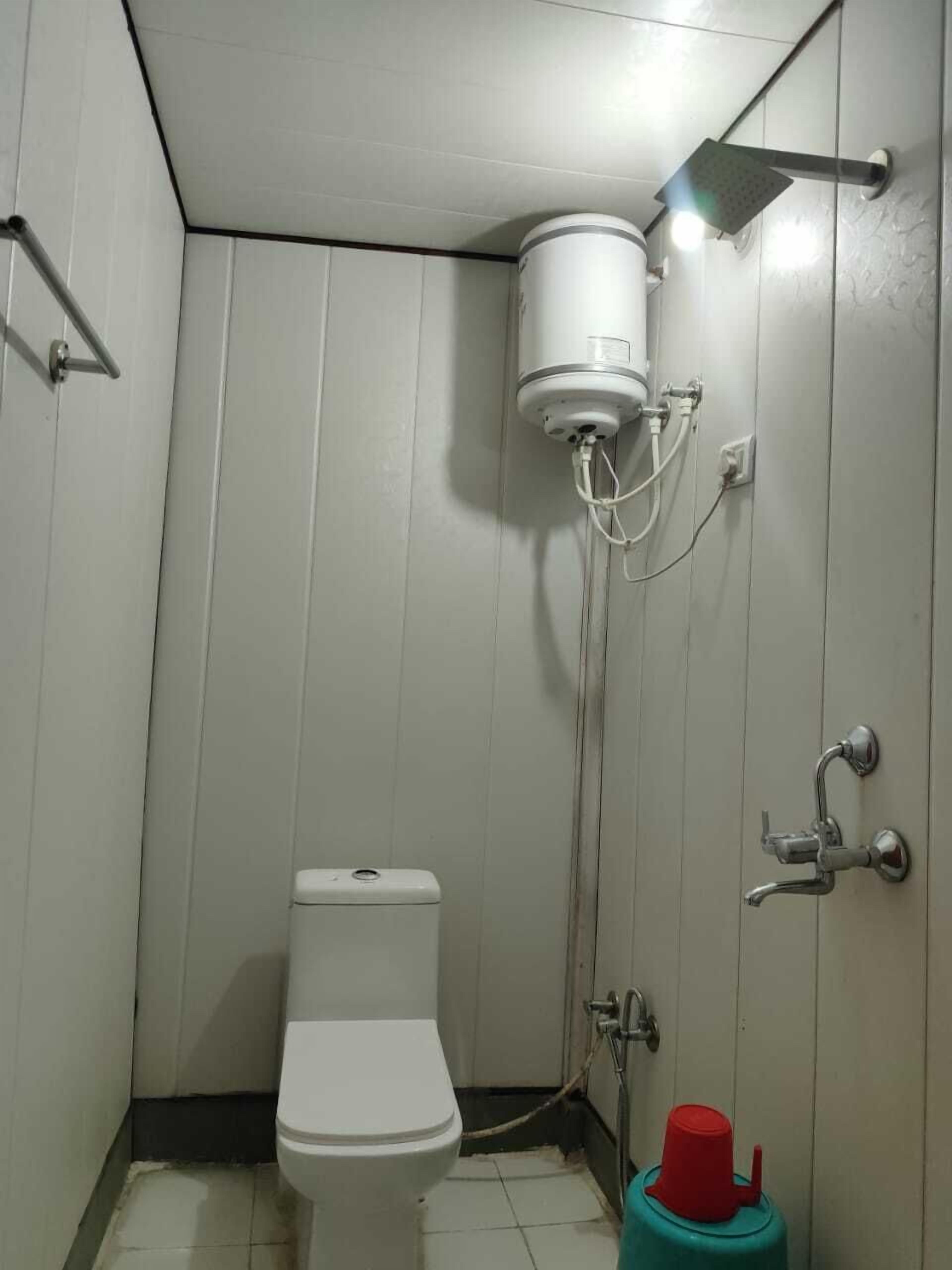A small, compact bathroom with a toilet, a shower unit, and a red water heater.