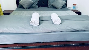 A neatly made bed with grey bedding and two rolled white towels, a dark headboard, and a bedside table with a vase and salt and pepper shakers. - New Mandakini River Resort (Ukhimath)