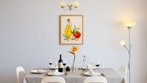 A dining room with a table set for four, a framed artwork above the table, and a floor lamp to the right. - Titou Apartment Sea View (Machico)