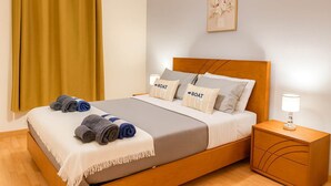 A neatly made bed with a headboard, a bedside lamp, and a wall-mounted artwork. - Titou Apartment Sea View (Machico)