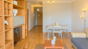 A modern living room with a wooden bookshelf, a dining area with a table and chairs, a sofa, and a decorative white statue on a table. - Titou Apartment Sea View (Machico)