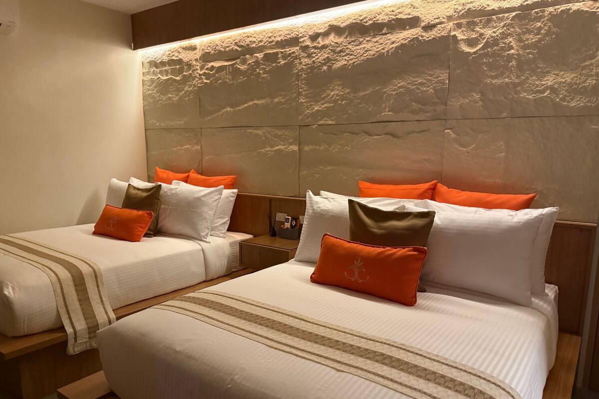Een hotelkamer met twee bedden, elk met wit beddengoed en oranje kussens. Het hoofdeinde heeft een gestructureerd stenen ontwerp.