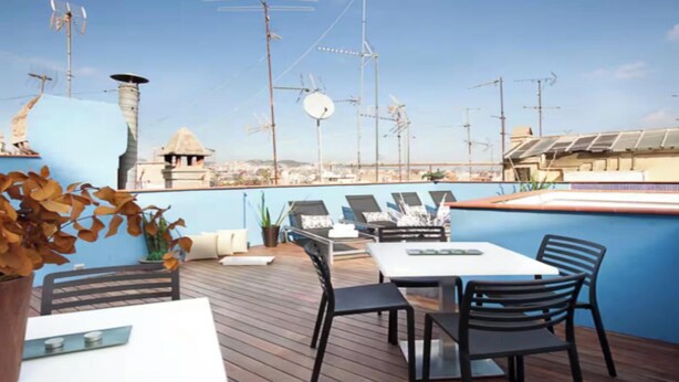 Terraço no telhado com mesa e cadeiras, vista da cidade e antenas.