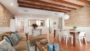 Uma sala de estar ampla com um sofá marrom, cadeiras brancas e uma mesa de centro de madeira.