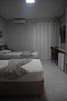 Habitación de hotel con dos camas, un escritorio, una silla, un refrigerador pequeño y una ventana con cortinas.